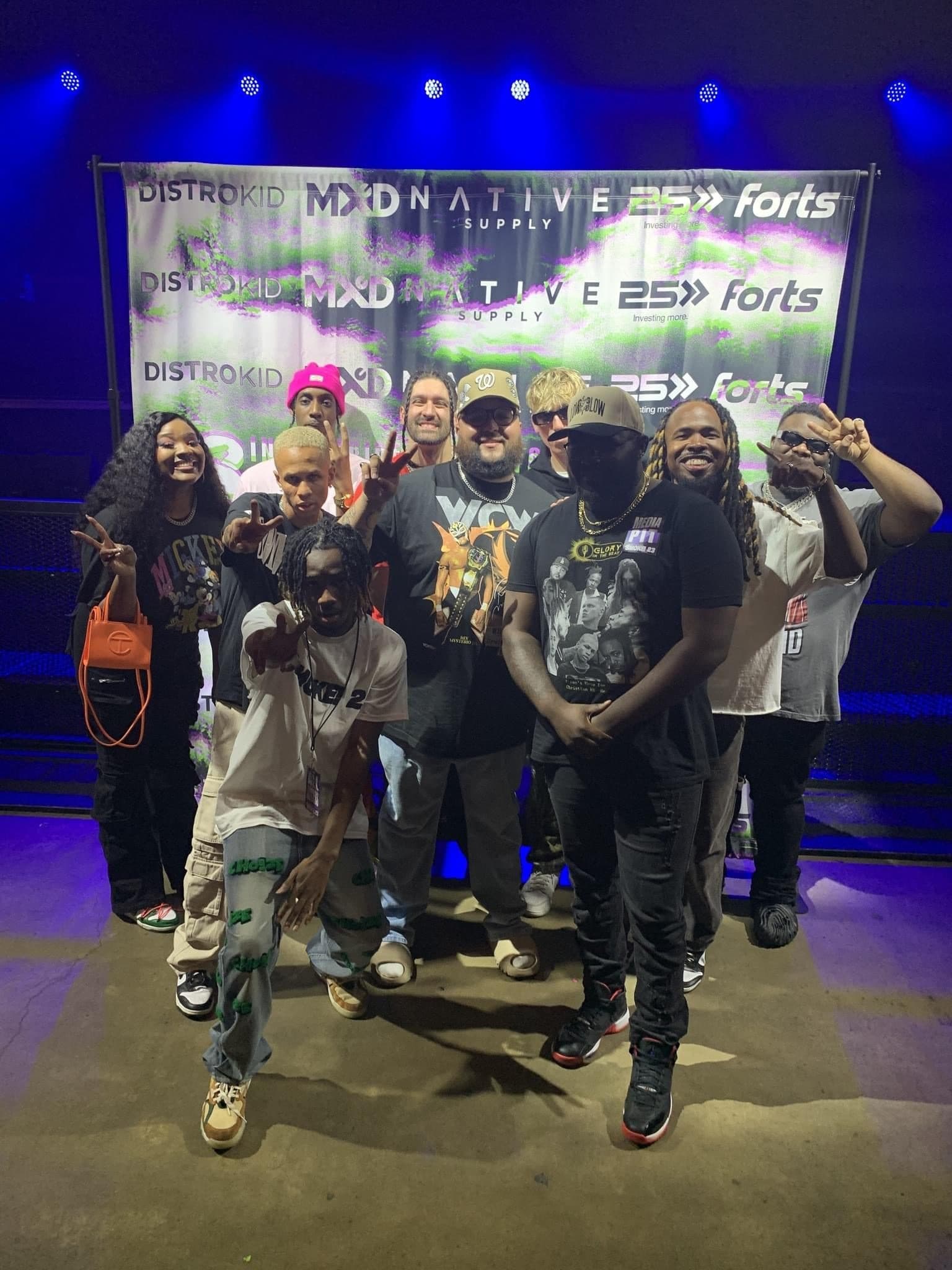 Artists and Glory in the Beat in front of a sponsor backdrop at a concert.