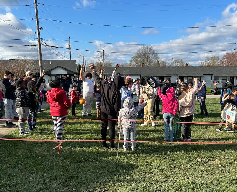 Niños y adultos levantan las manos en adoración en un encuentro comunitario al aire libre.